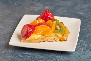 Portion of a delicious fruit and cream cake on a square white plate.