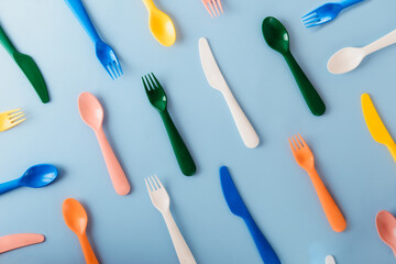 The pattern of reusable cutlery on the blue background. Plastic spoons, forks, knives top view. Summer Picnic. Plastic recycle concept.