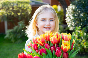 Cute adorable smiling toothless little girl with a huge bunch of tulips. Girl getting flowers. Picking flowers for gift bouquet in the garden. Mother's day, Birthday surprise. Happy childhood.