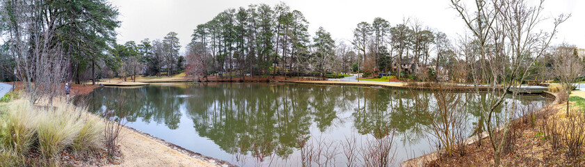 a stunning shot of vast green lake water with lush green and autumn colored trees and yellowish brown grass on the banks of the lake  at The Duck Pond Park in Atlanta Georgia