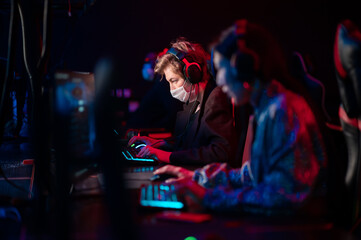 Training bootcamp for professional esports players. Young cyber-athletes play an online shooter game. Glowing keyboard, neon light.