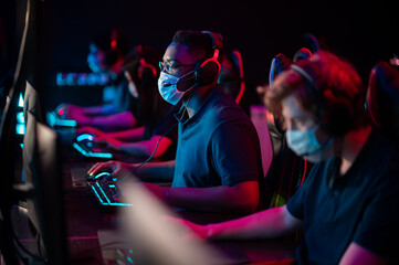 White-skinned and black-skinned guys are members of an esports online strategy crew. Play at the computer at an international tournament during the pandemic.