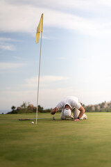 Angry golfer lamenting for missing his shot on the green a few inches from the hole.