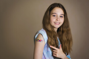 Happy teenage girl vaccinated against coronavirus rolls up her sleeve and points to the vaccination...