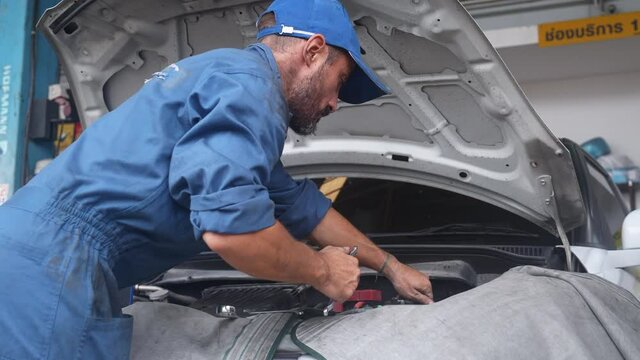 Young man is mechanic repairing engine of car in the garage, auto service, worker fix and adjusting part of automobile with problems in the station, transportation and automotive concept.