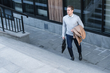 Tired office worker climbs stairs, holding coat in one hand and business case in the other. end of working day.