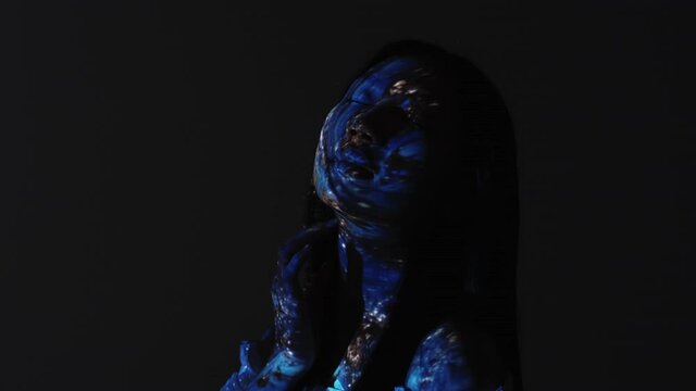 Exotic beauty. Fantasy portrait. Mystic goddess. Universe wisdom. Silhouette of peaceful relaxed alien woman touching blue glitter face in projector light motion isolated on dark.