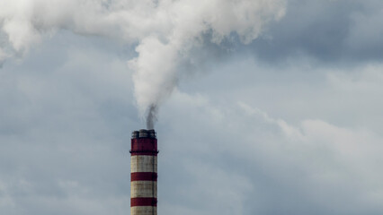 Industrial smoke from chimney on dramatic sky background. View of high chimney pipes with grey smoke from coal power plant. Production of electricity with fossil fuel. Wind blowing pollution.
