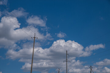 Electric poles against a summer blue sky with cumulus clouds.