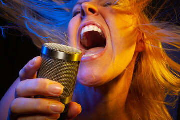 Female vocalist under gelled lighting sings with passion into condenser microphone.