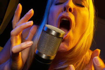 Female vocalist under gelled lighting sings with passion into condenser microphone.