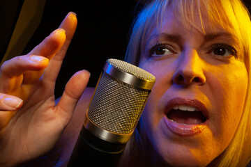 Female vocalist under gelled lighting sings with passion into condenser microphone.