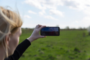 Woman photographs nature scenery on smartphone. Close up of defocused woman's face and hands. Phone. Mobility and modern lifestyle concept. Beautiful sky. Young girl taking pictures of the landscape