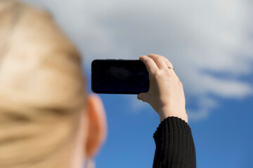 Woman photographs nature scenery on smartphone. Close up of defocused woman's face and hands. Phone. Mobility and modern lifestyle concept. Beautiful sky. Young girl taking pictures of the landscape