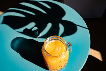 fresh orange juice in summer light and monstera or split-leaf philodendron leaves