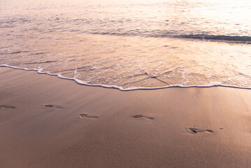 Footprints in the sand by the sea. In the light of the sunset, the footprints follow the sand along the surf.