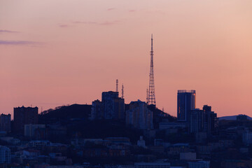 Fototapeta na wymiar Dawn in Vladivostok. The Vladivostok TV tower stands on a hill among residential buildings in the city center. City built-up hill at dawn.