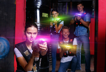 Portrait of young positive cheerful smiling girl took aim colored laser guns during laser tag game in labyrinth