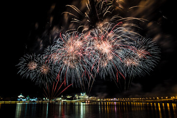 bright festive fireworks with beautiful flowers bloom over the river on a warm clear evening