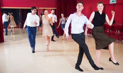 Young smiling people practicing vigorous jive movements in dance class