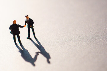 Silhouettes of two businessman, probably men, shaking their hands as a sign of an agreement or...