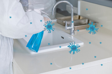 A healthcare worker in a white protective suit using blue chemical fluid to disinfect the surface of a wash basin.