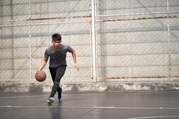 young asian man basketball player attempting a dunk outdoors