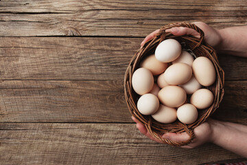 Hands holding basket with organic chicken eggs on wooden background