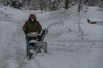 Man operating a snow thrower in a rural setting on a snowy day