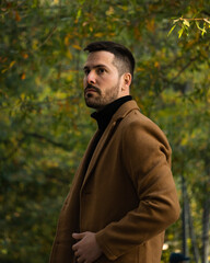 Fall portrait of a bearded man with a brown coat at sunset time in the park