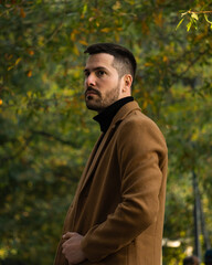 Fall portrait of a bearded man with a brown coat at sunset time in the park