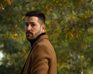 Fall portrait of a bearded man with a brown coat at sunset time in the park