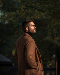 Fall portrait of a bearded man with a brown coat at sunset time in the park