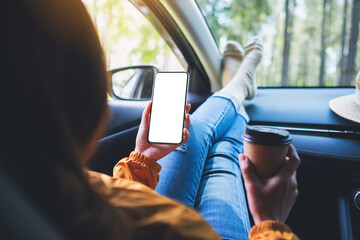 Mockup image of a woman holding and using mobile phone with blank screen while drinking coffee and...