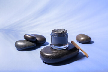 Jar of cosmetic clay and spa stones on color background