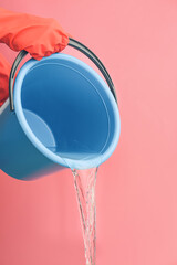 Woman pouring water from bucket on color background © Pixel-Shot