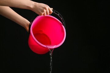 Woman pouring water from bucket on dark background © Pixel-Shot