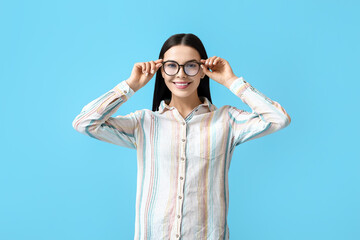 Beautiful young woman wearing eyeglasses on color background