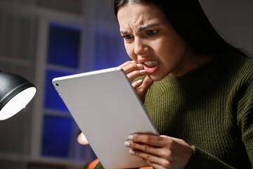Stressed young woman with tablet computer at home late in evening. Concept of addiction