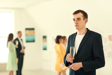 Naklejka na ściany i meble Young man drinking champagne at exhibition in modern art gallery