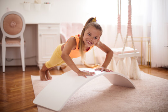 Little Girl Doing Push-ups In The Bedroom At Home.