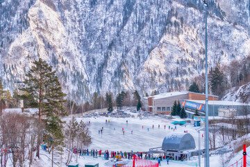 Ice skating rink between the snowy, wooded mountains. Winter. Translation: 