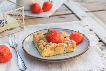 Piece of rhubarb crumble cake and strawberries on a plate on a wooden table