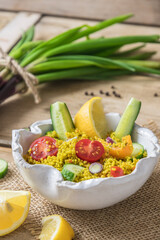 Couscous salad with cucumber, tomatoes and onions in a white bowl on rustic wooden background, vertical