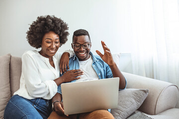 Young couple sitting in their living room with laptop waving to their marital therapist after successful online therapy and saved marriage. Shot of a smiling young couple using a laptop while relaxing
