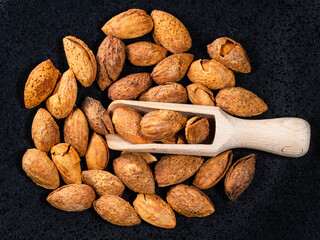 top view of wooden scoop in cracked almond drupes