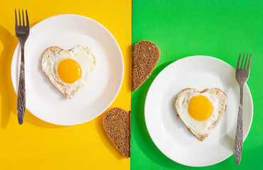 top view of two heart-shaped scrambled eggs with toasts, a pair of fried eggs on white plates on yellow and green background, romantic minimalistic design, healthy breakfast for sweetheart