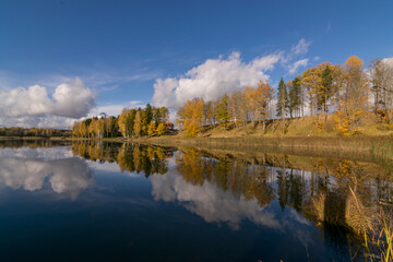 Fototapeta premium colorful autumn panoramas with yellow trees by the lake, beautiful and colorful reflections of trees and clouds in the calm lake water