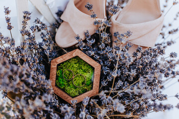 Two wedding rings in a wooden box with a moss plant on a purple lavender flowers background