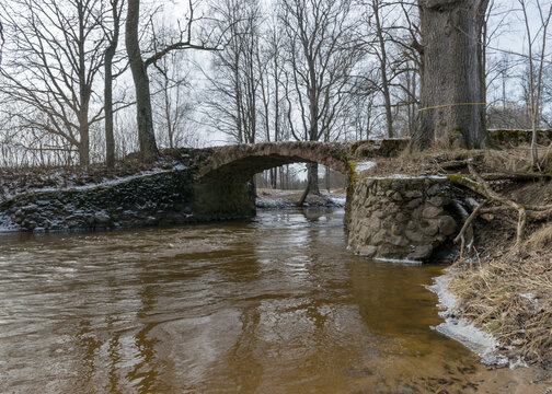 a continuous boulder stone bridge with a brick used for masonry, early spring, bare trees, snow plan on the ground, Stone arch bridge over the river Kuja, Madona, Latvia